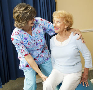 Physical therapist helps a senior woman exercise using a pilates ball.