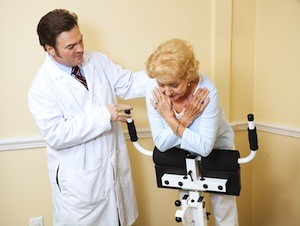 Chiropractor supervises a senior woman as she uses a Roman Chair to stretch her spine. Authentic and accurate content depiction.